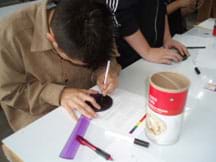 A student cuts a hole in the lid of the oatmeal container using an Exact-o knife.