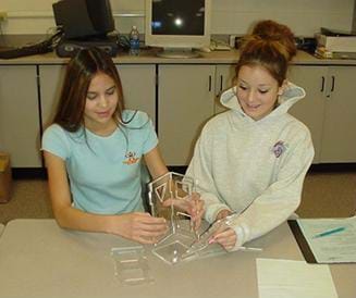 A photo shows two female teens building their acrylic tower.