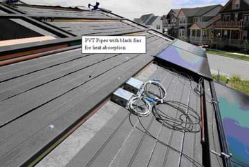 Photo shows flat plastic pipes covering an angled roof surface with two shiny black panels installed over some of them, plus some wires and electrical outlet boxes. A labeled arrow says: PVT pipes with black fins for heat absorption.