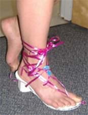 A photograph shows a girl's foot in a strappy heeled shoe made of foam core and ribbons.