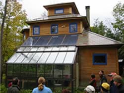 A photograph shows people standing outside a two-story house with one side looking like an attached greenhouse (lots of glass).
