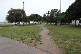 A dirt path crosses a green park between two established paved paths.