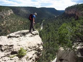 A person in hiking gear stands at the edge of a cliff overlooking a canyon.