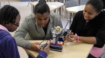 Photo shows three teens around a table working on a LEGO robot.