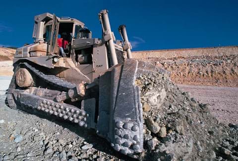 Photo shows a heavy industrial bulldozer pushing a massive amount of rocky soil.