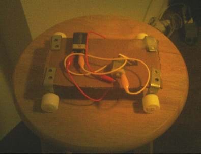 Photo shows a model vehicle made with cardboard, L-brackets, wires, alligator clips, a 9-volt battery, and wheels. 