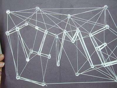 Photo shows a web that spells out TIME made from white string wrapped around push pins poked into a black board.
