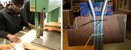 Two photos: A student wearing safety goggles uses a band saw to cut a flat piece of material. An open-topped L-shaped wooden box zip-tied to a crutch below the hand hold. The big part of the box holds a notebook; the small part of the box holds pencils.