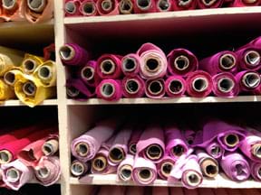 Photograph shows shelves full of cylindrical bolts of fabric.