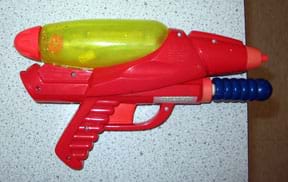 Photo shows a red gun-shaped toy laying flat on a table with its nozzle pointed off the table edge.