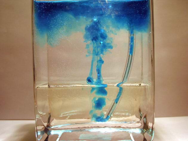 Photo of corn syrup on bottom of container and water on top with the syringe and tube inserted into the bottom of the container with blue dye rising up from end of tubing. Photo of corn syrup on bottom of container and water on top with the syringe and tube inserted into the bottom of the container with blue dye rising up from end of tubing.