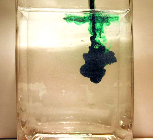 Photo shows plume of green food coloring dropping deep into water in a glass container. Photo shows plume of green food coloring dropping deep into water in a glass container.