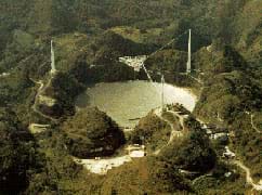 Photo shows a huge dish inset into a forested valley, with structures and towers around it.