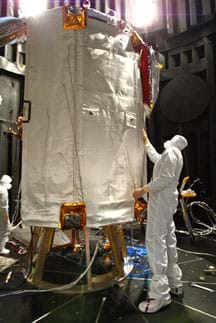 A man in a white jumpsuit examines the white material covering a structure about 3m high x 2m wide in size.