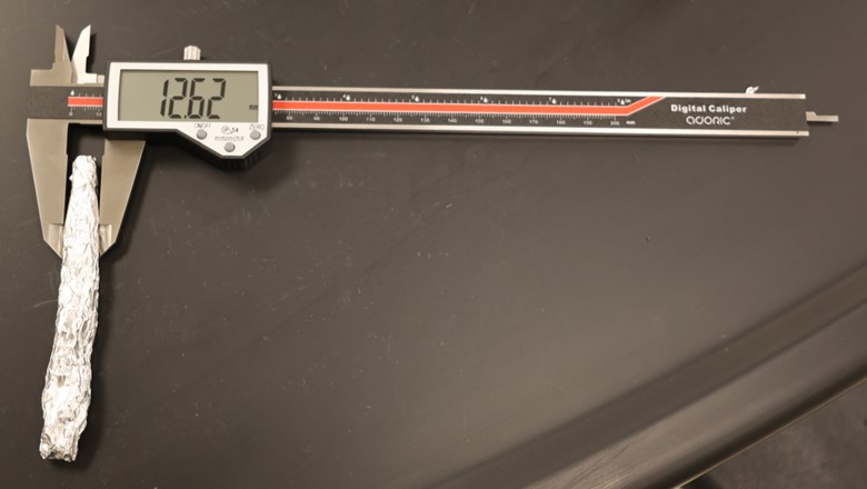 A photo showing aluminum foil that has been wrapped up into a cylinder, with calipers being used to measure the diameter.