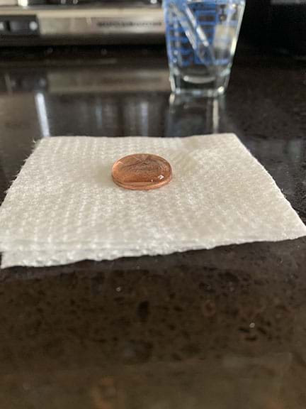 A penny on a paper towel with water on the penny. The water is in a dome shape.