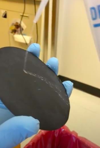 A gloved hand is holding a round disk and water is being squirted on the disk.  Water bounces off the disk in a stream.