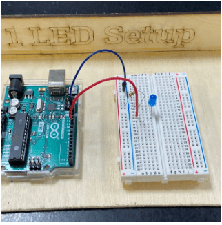 Photo showing a breadboard with a blue LED, resistor, and Arduino wired in series. 