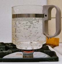 Photo shows a clear pot of bubbling water on a gas stove burner.