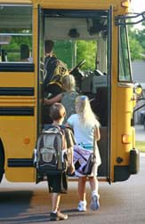 Photo shows four young students climbing onto a school bus.