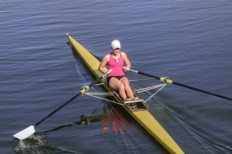 Photo shows one female rowers working hard as she pulls on paddles to power a boat.