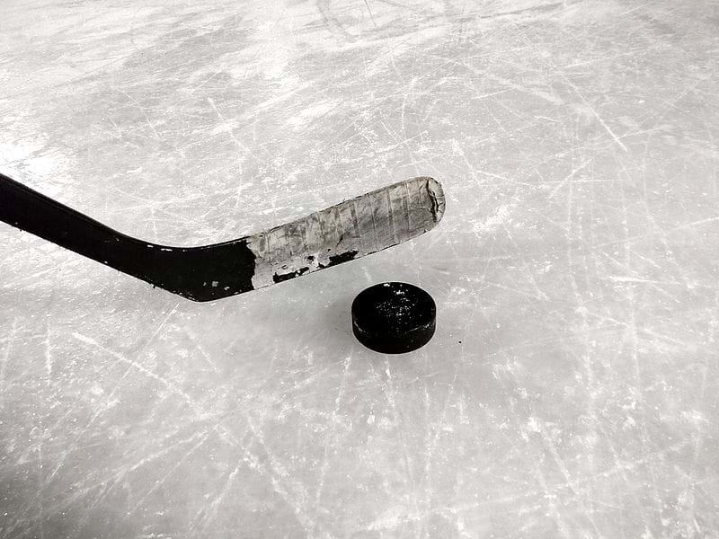 An image shows a hockey stick and hockey puck resting on a scratched ice rink. 