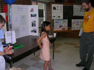 In front of a poster board, a student describes her energy project to an adult. 
