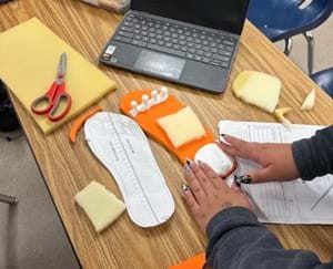 A photo of a student using their hands to form a moldable foam on top of an orange orthotic shoe insole.