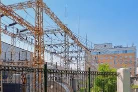 A photo of an electrical substation with numerous powerlines leading into metropolitan city.