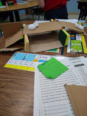 A student gluing sponges to cardboard to create bridge and underpass.