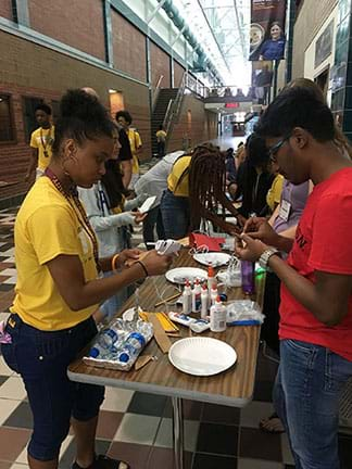 Students use glue and other adhesive material at a table to construct their boats.