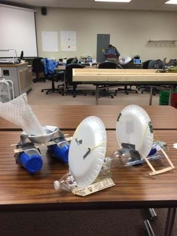 Three examples of final student boat designs sit on a classroom table.