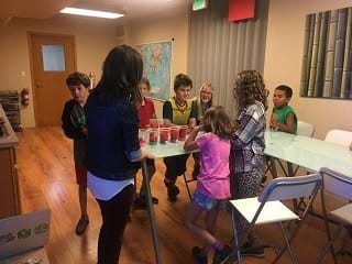 A picture of 5 students standing around a table with 4 cups filled with pom poms on the table.
