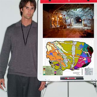 A photograph shows a young man standing by an easel with a poster-sized cavern photo and map on it.