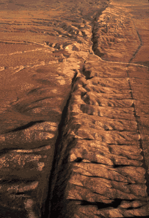 An aerial photograph shows a dry terrain of hills and canyons spreading out from a spine-shaped crack in the Earth's crust.