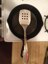 A close up of an iron skillet with a metal spatula resting on it.