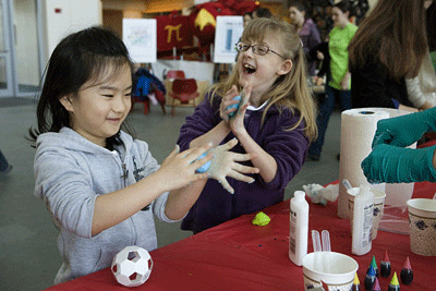 Photo shows two young girls laughing and smiling as they roll blue imitation silly putty in their hands. 