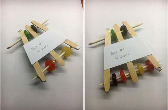 Two photos show two tests of a mint-mobile. Left: A mint-mobile made out of popsicle sticks and wooden dowels has four multi-color wheels, an index card taped to the car reads, “Test #1, 4 wheels.” Right: The same mint-mobile now has six multi-color wheels, two in the front and four in the back, an index card taped to the car reads, “Test #2, 6 wheels.”