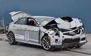 A photograph shows a silver sedan after a vehicle crash test, with a good view of the front and passenger sides of the vehicle. The hood, bumper, grill, and engine are smashed and crumpled. The front passenger air bag and window air bag have been deployed. The trunk is open.