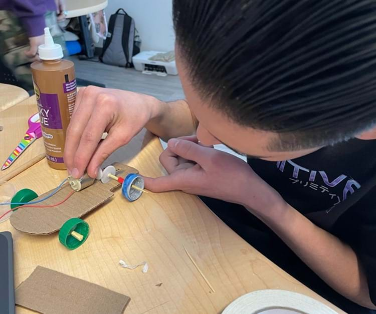 A student aligning gears on a model electric vehicle.