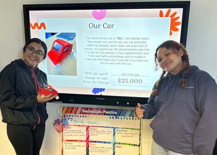 Two students standing in front of a screen presenting their model EV during the Design Expo.