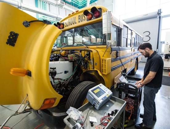 An electric yellow school bus is being analyzed by an NREL engineer using a computer to assess its vehicle-to-grid functionality.
