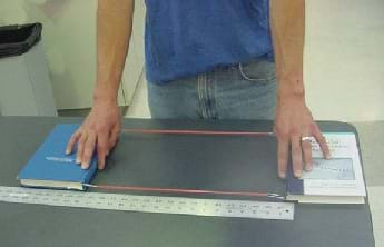 A photo shows a student holding two books apart, just before they are released.  The books are attached to one another via a sling-type setup made with rubber bands and paperclips.