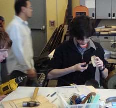 Photo shows a student at a classroom workbench attaching the heel to a shoe. 