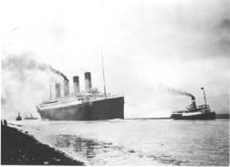 Black and white photo shows a big ship with four smokestacks moving through the water.