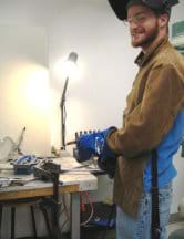 A teenager wears gloves and a protective mask as he works at a machine shop bench with good lighting