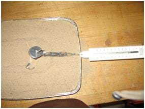 Photo from above the activity set-up shows a pan of sand on a table with a popsicle-stick device connected to a spring scale as it is pulled across the pan.