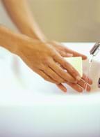 Photo shows hands with bar of soap under a stream of water in a sink.
