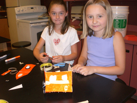 Photo shows two girls at a table with supplies.