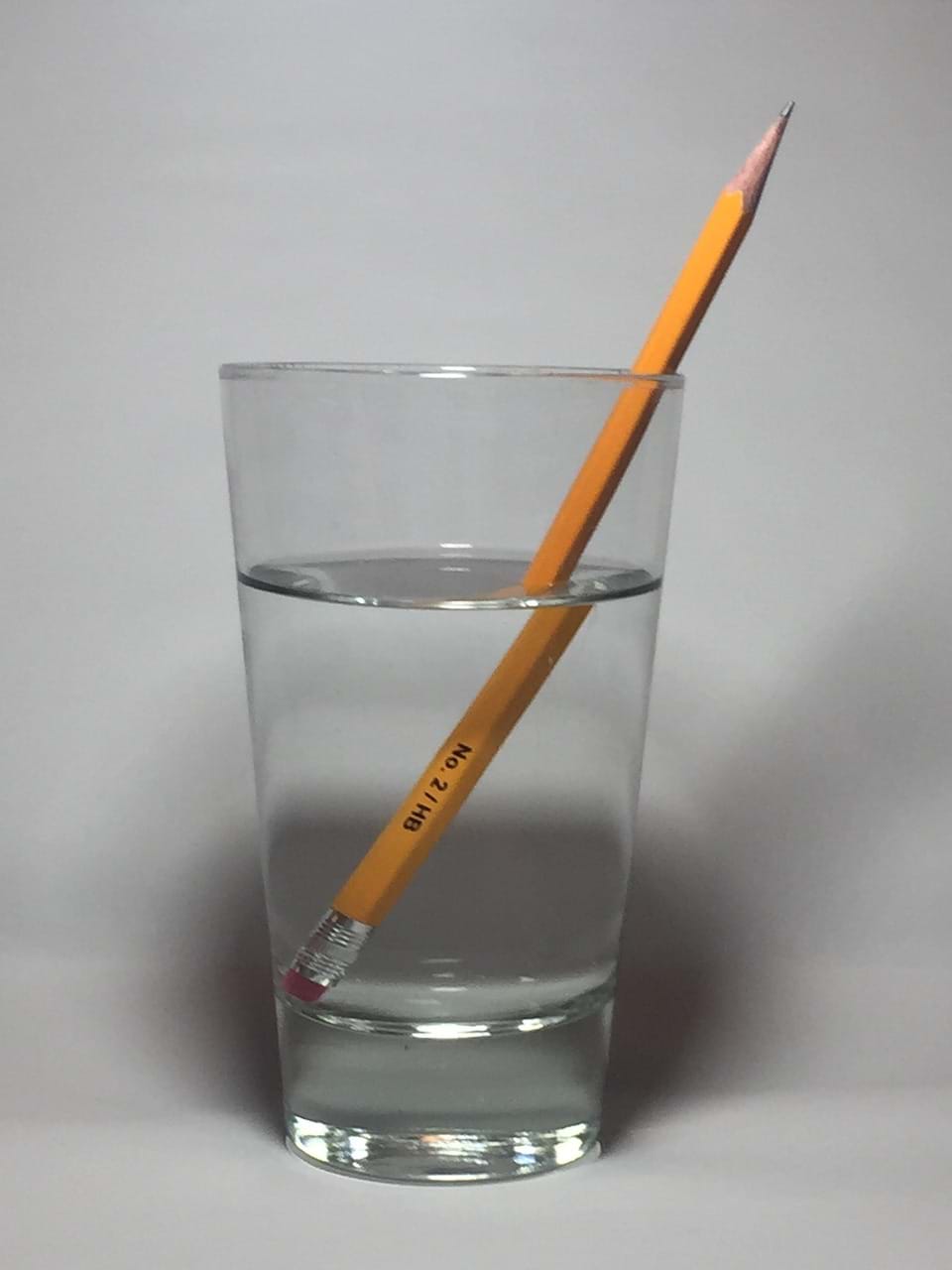 Photo of a pencil in a glass of water. The pencil image is refracted at the point where the pencil enters the water.